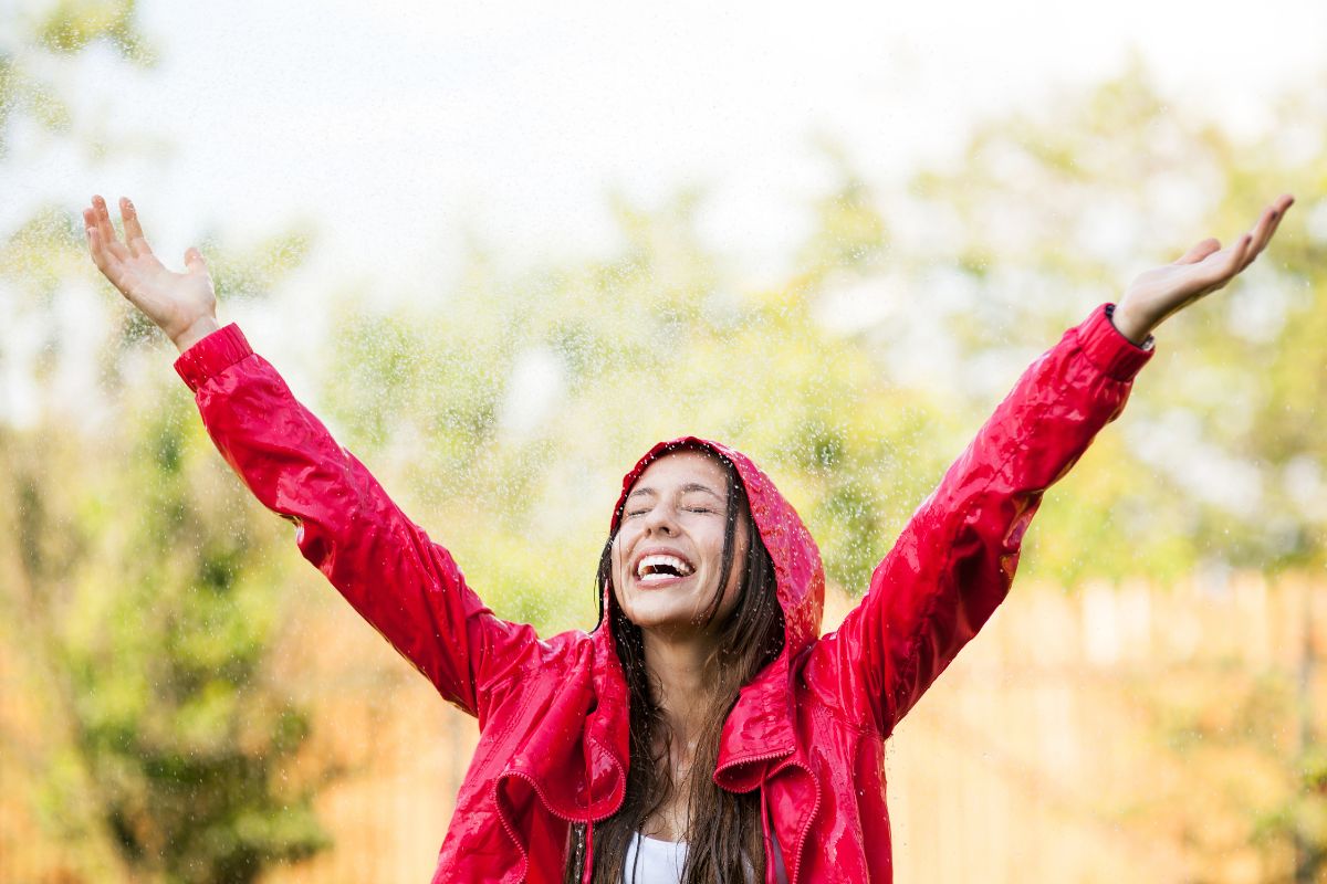 Woman in red rain jacket enjoying spring time rain shower.