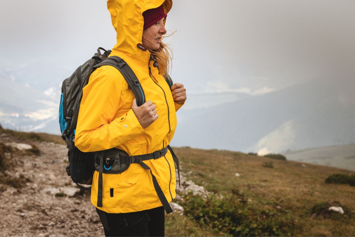 Woman hiking in the mountains in extreme weather. Tourist wearing waterproof jacket with hood. Sportswear and backpack.