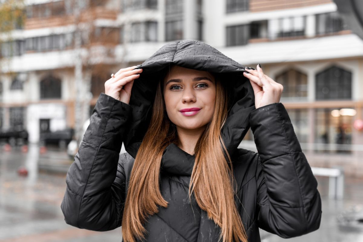 beautiful girl with makeup in a black jacket in a hood in the rain