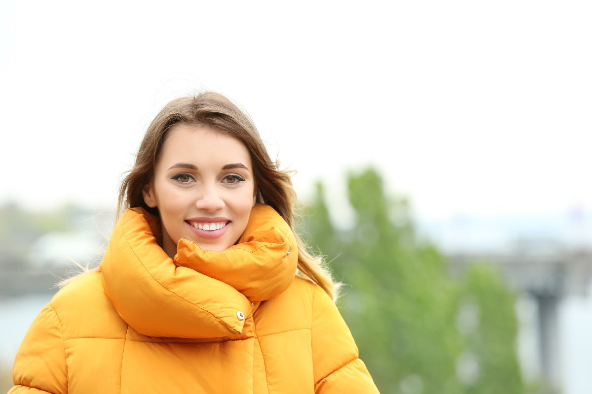 Attractive smiling woman in orange puffer jacket outdoors.